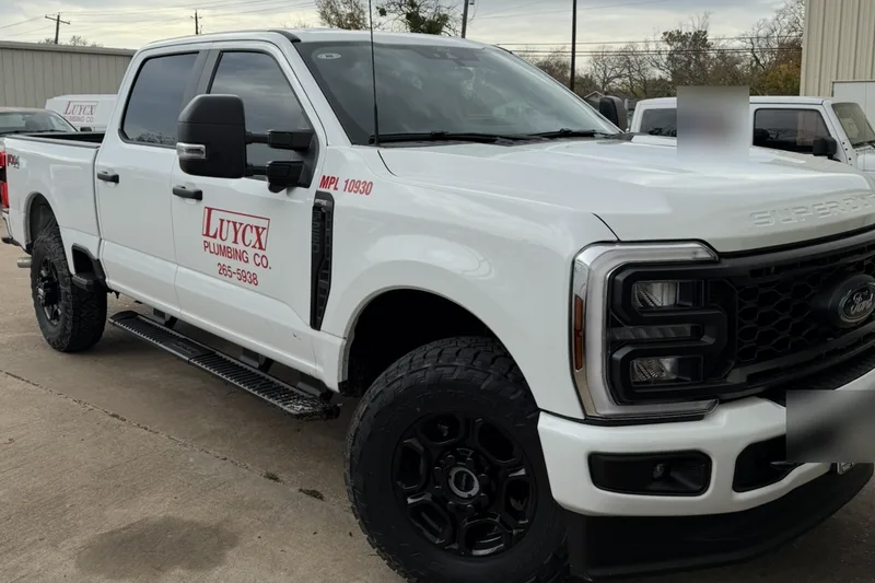 A newer white Luycx Plumbing Co. crew-cab truck with the same red lettering